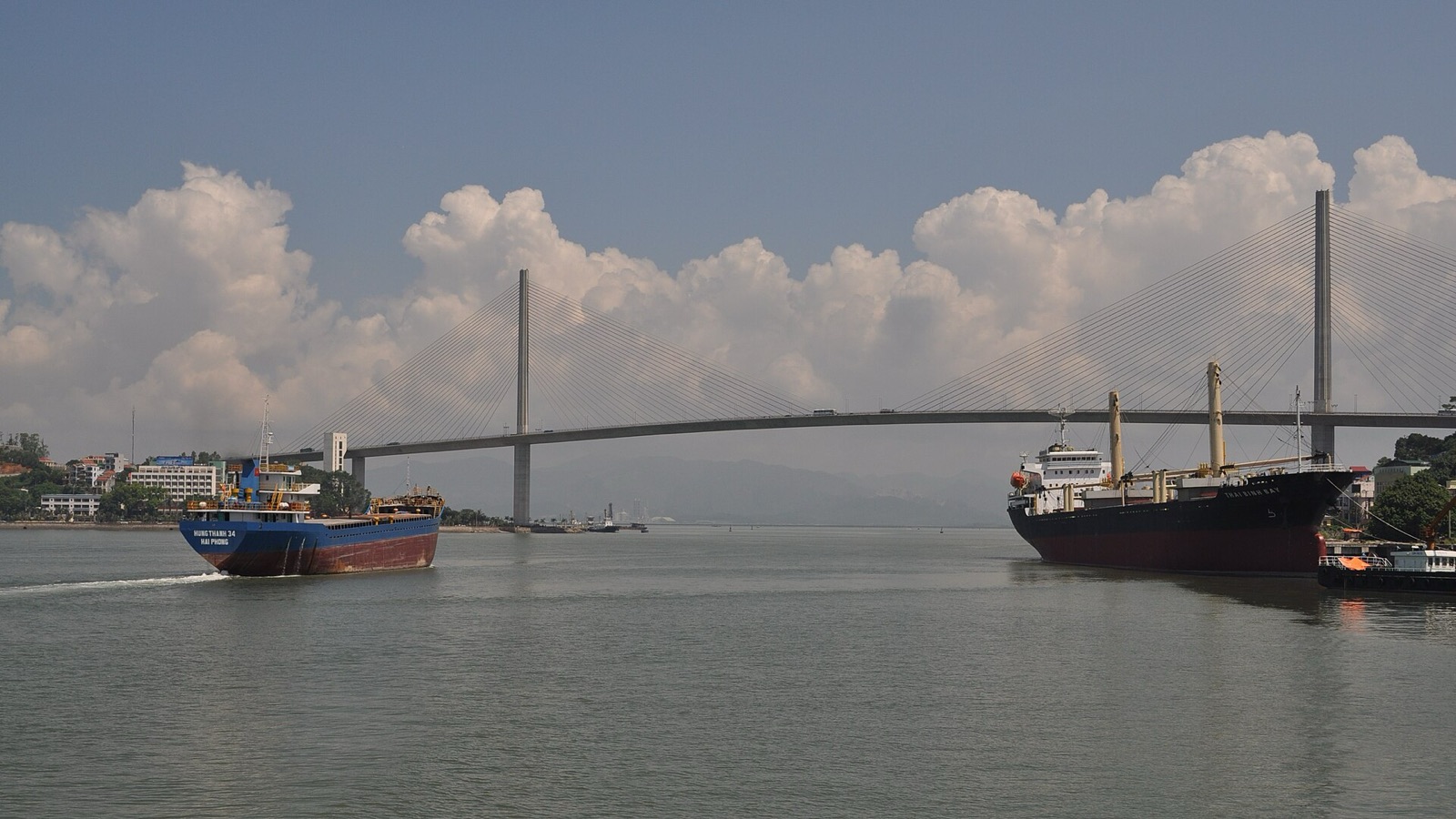 The cable-stayed Bai Chay Bridge spanning the water in Ha Long city on a sunny day, with two cargo ships passing below