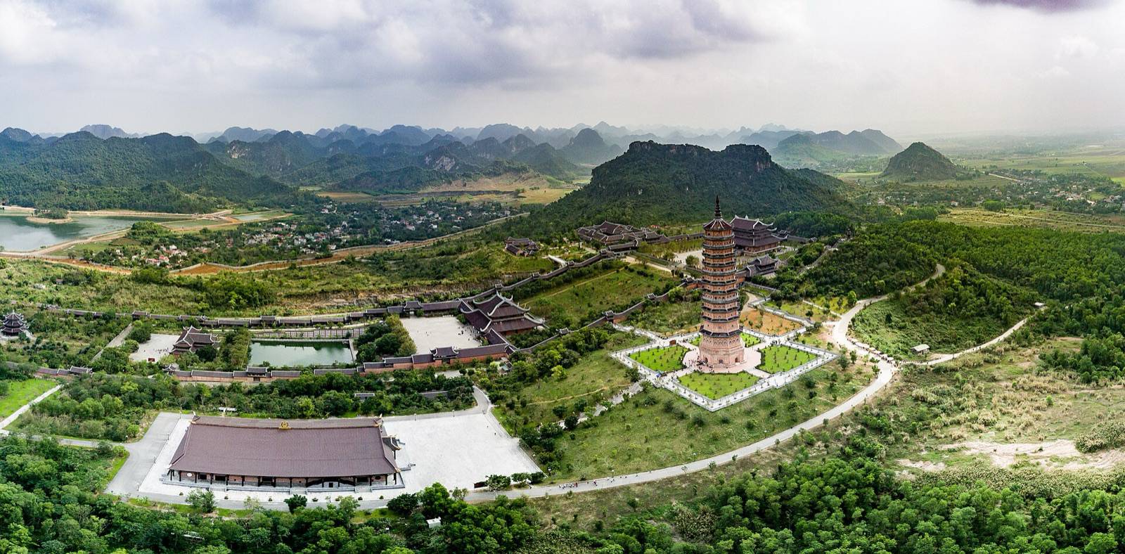 Aerial view of Bai Dinh Pagoda's tall stupa and temple halls among green hills and limestone peaks in Ninh Binh on a bright day