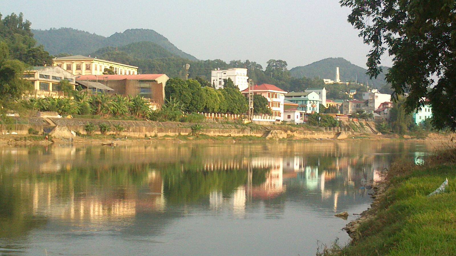 Riverside buildings and green hills of Cao Bang city reflected in the calm Bang Giang River on a sunny day