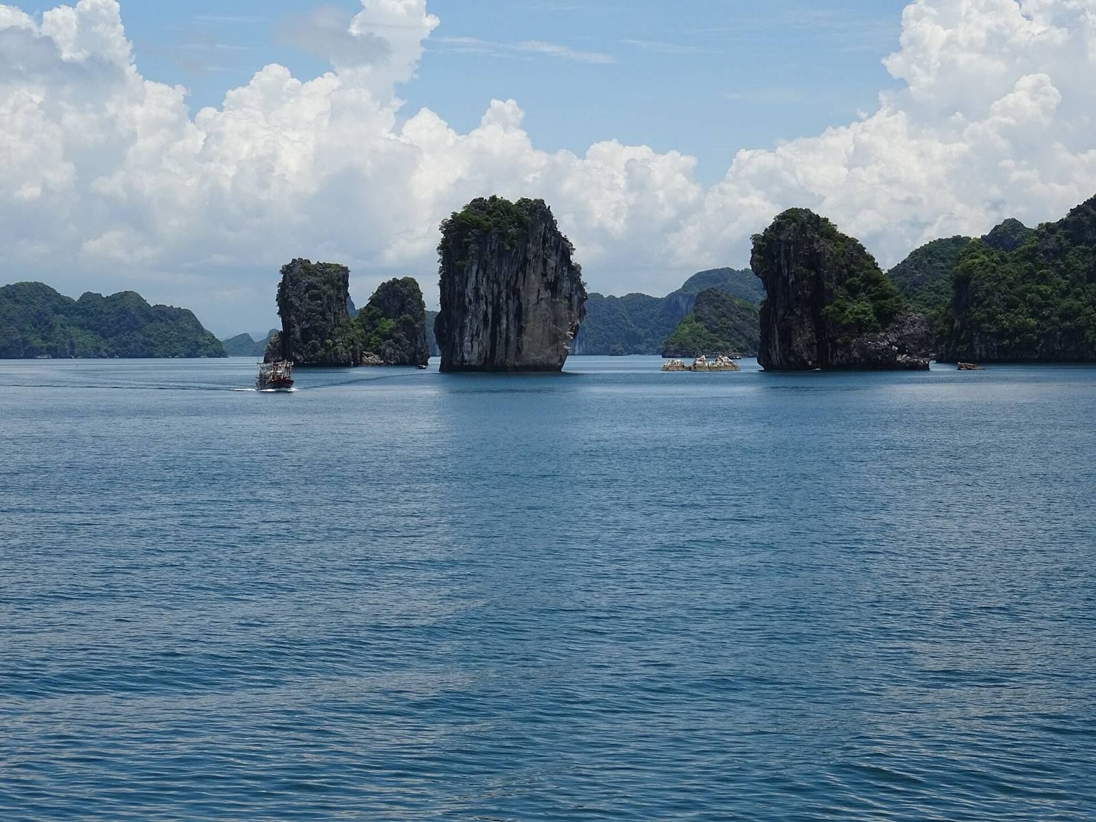 Limestone karst islands rising from blue water in Ha Long Bay under a bright sky with white clouds