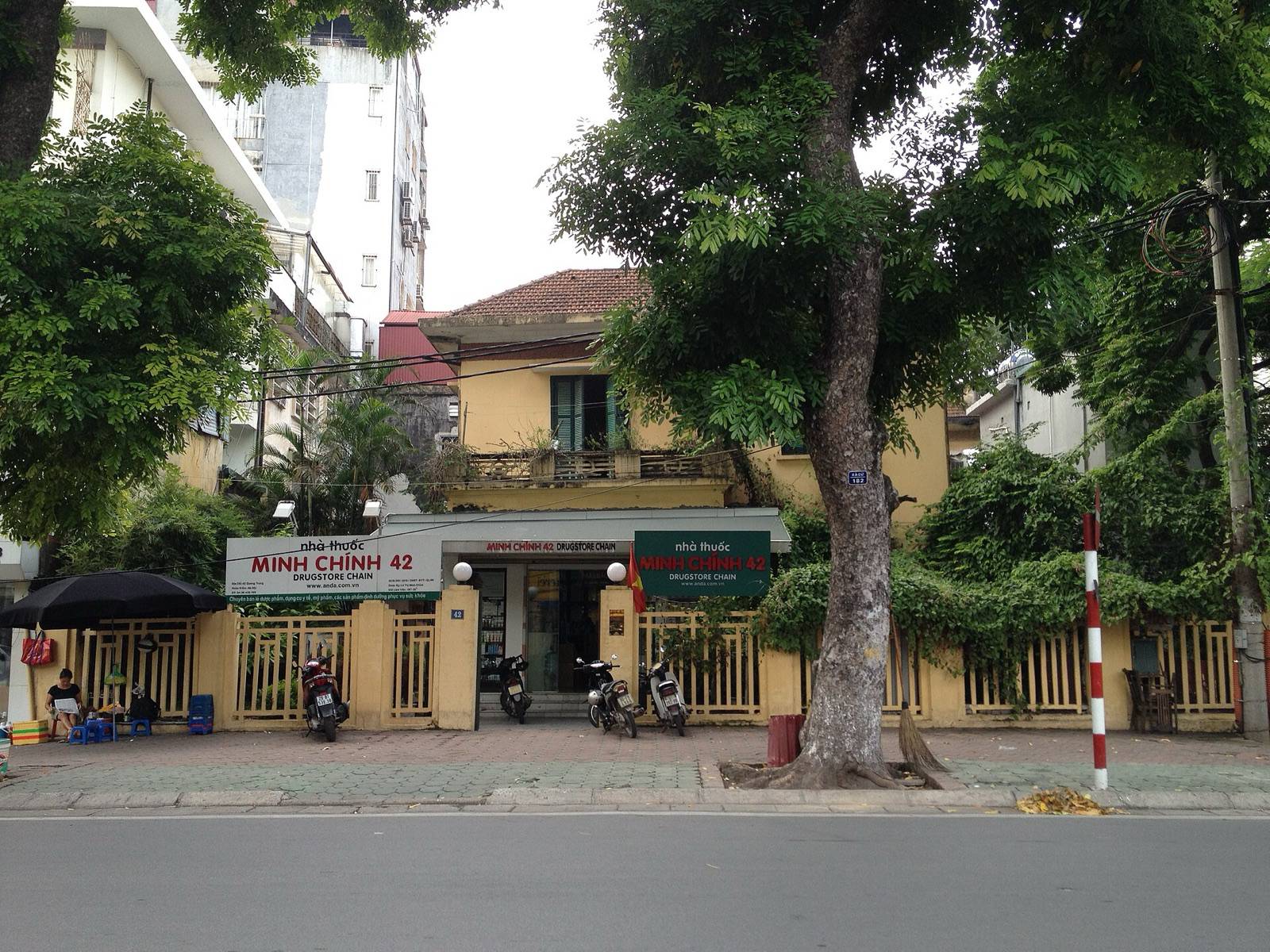 A nha thuoc pharmacy with green and white signs in front of a yellow two-story villa on a tree-lined street in Hanoi