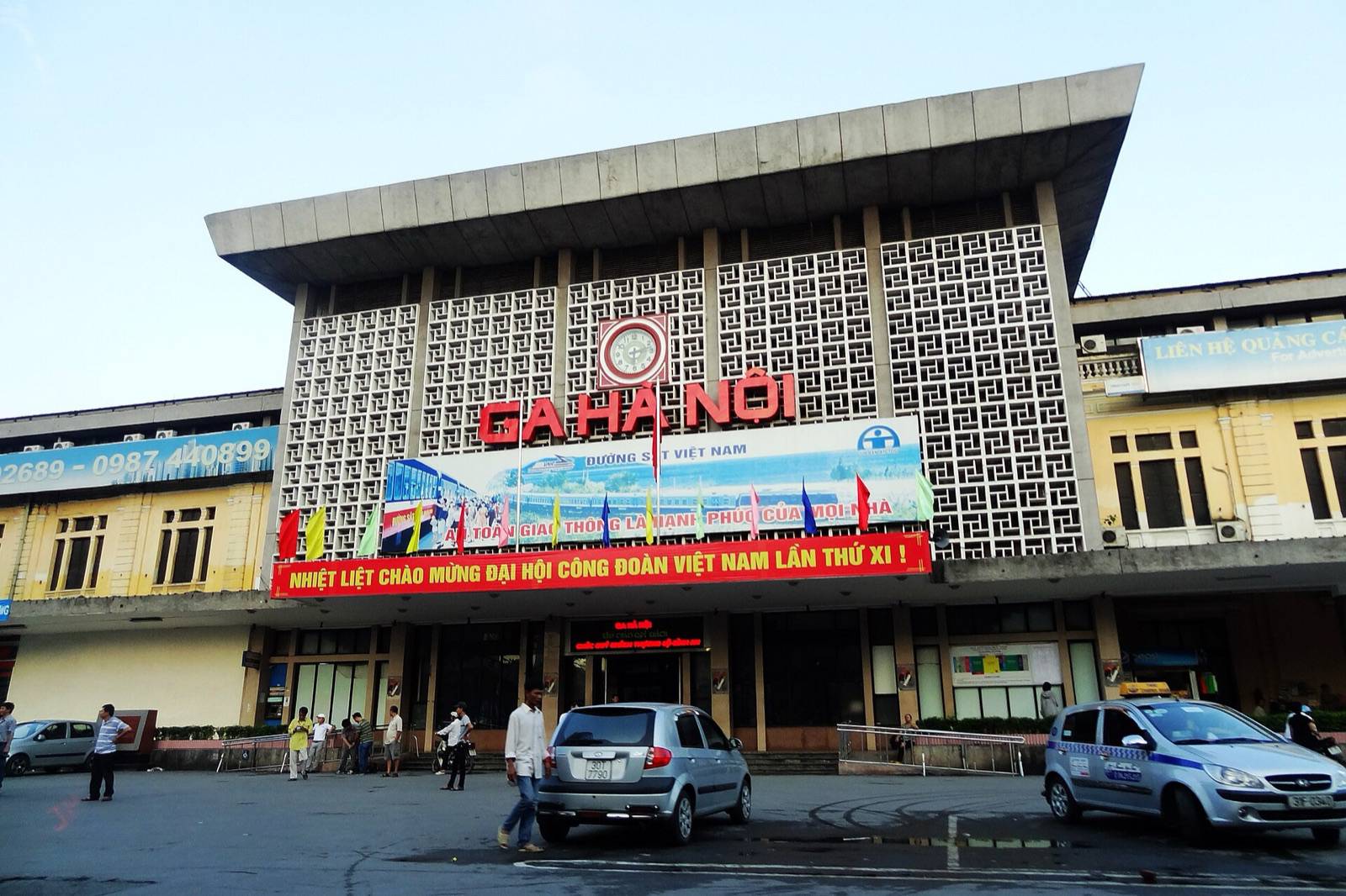 The front of Hanoi Railway Station on Le Duan street, with its red GA HA NOI sign and clock under a clear morning sky