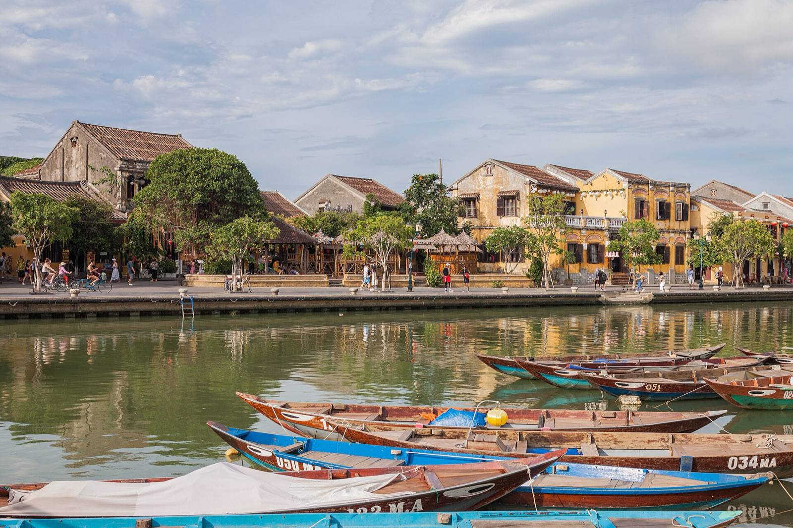 Wooden boats moored on the river in front of the yellow shophouses of Hoi An Old Town on a sunny afternoon