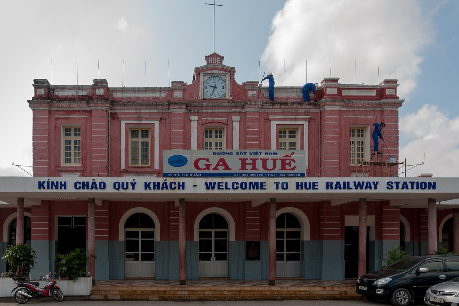 The pink colonial-era facade of Hue Railway Station, with its Welcome to Hue Railway Station sign under a blue sky