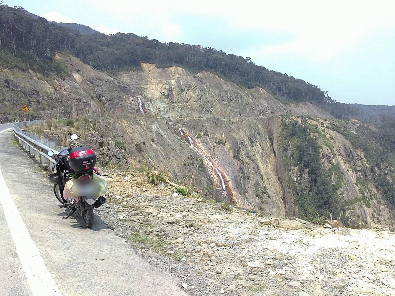 The Khanh Le Pass road between Nha Trang and Da Lat cut into steep mountain slopes, with a waterfall below on a bright, hazy day
