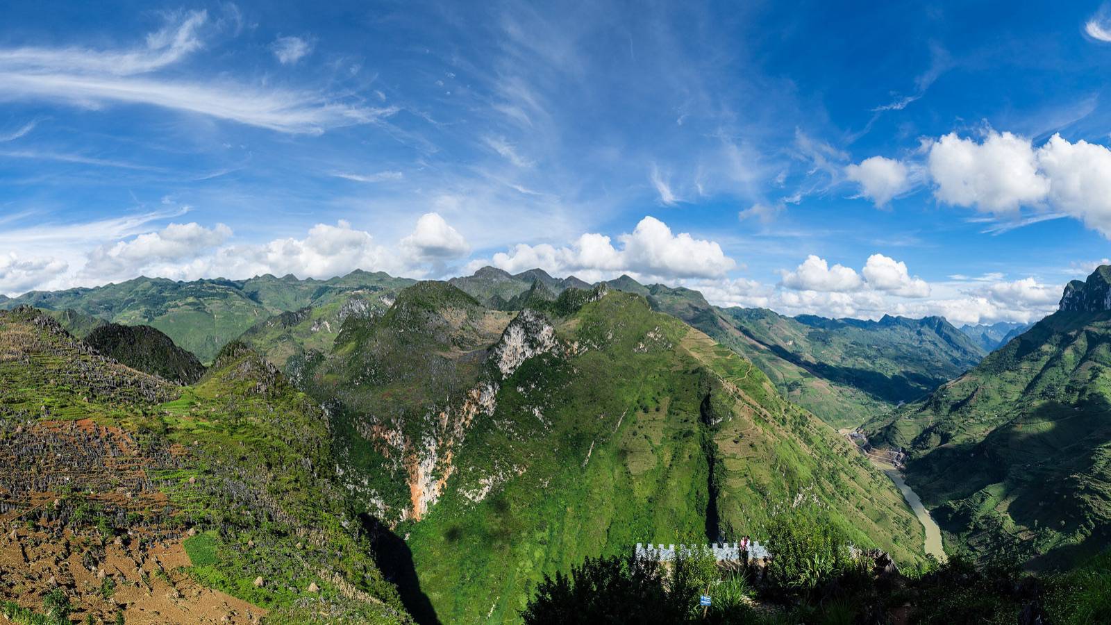 Green karst mountains and the deep Nho Que River gorge seen from Ma Pi Leng Pass on the Ha Giang Loop under a bright blue sky