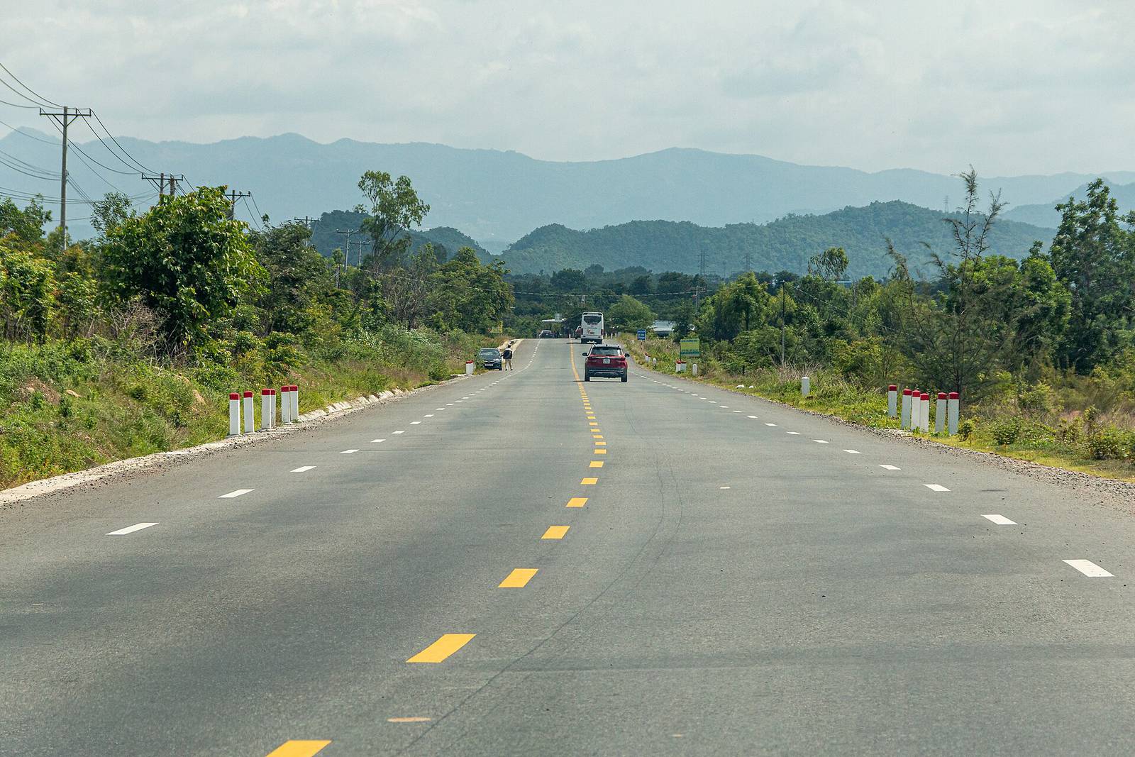 The freshly paved Highway 28B between Da Lat and the coast, with a coach and a car on the road and forested mountains ahead on a bright, hazy day