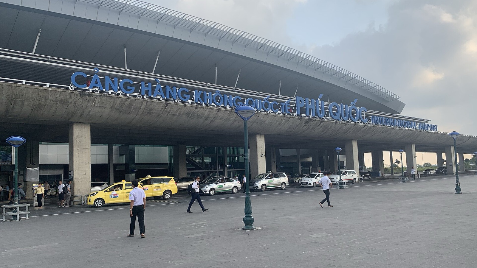 The front of Phu Quoc International Airport with its blue Cang Hang Khong Quoc Te Phu Quoc sign, taxis and travelers in daylight