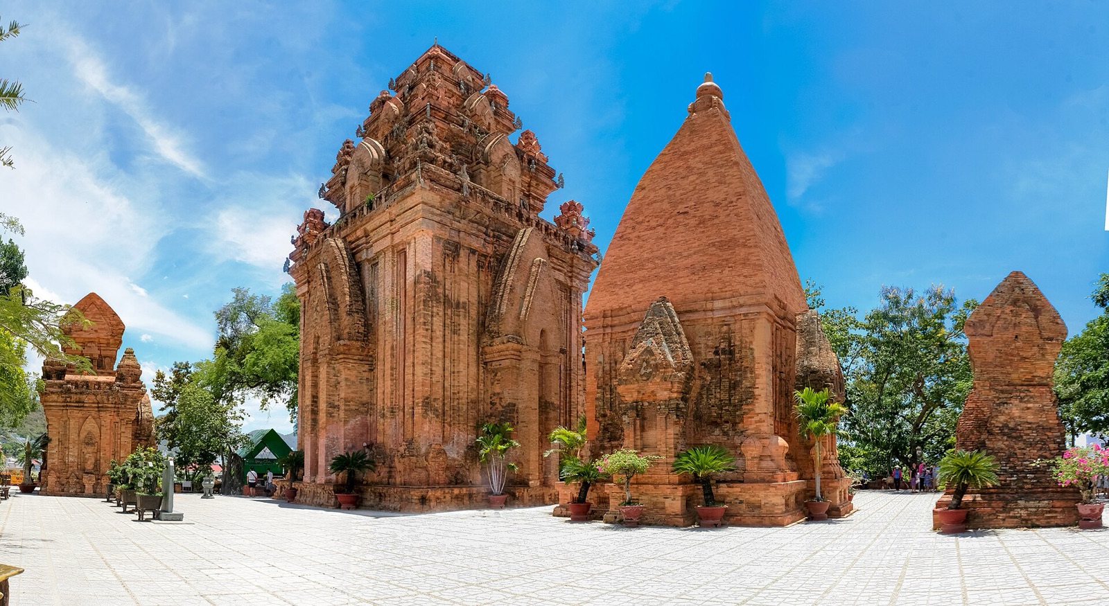 The red brick towers of the Po Nagar Cham temple in Nha Trang under a bright blue sky, with potted palms on the stone courtyard