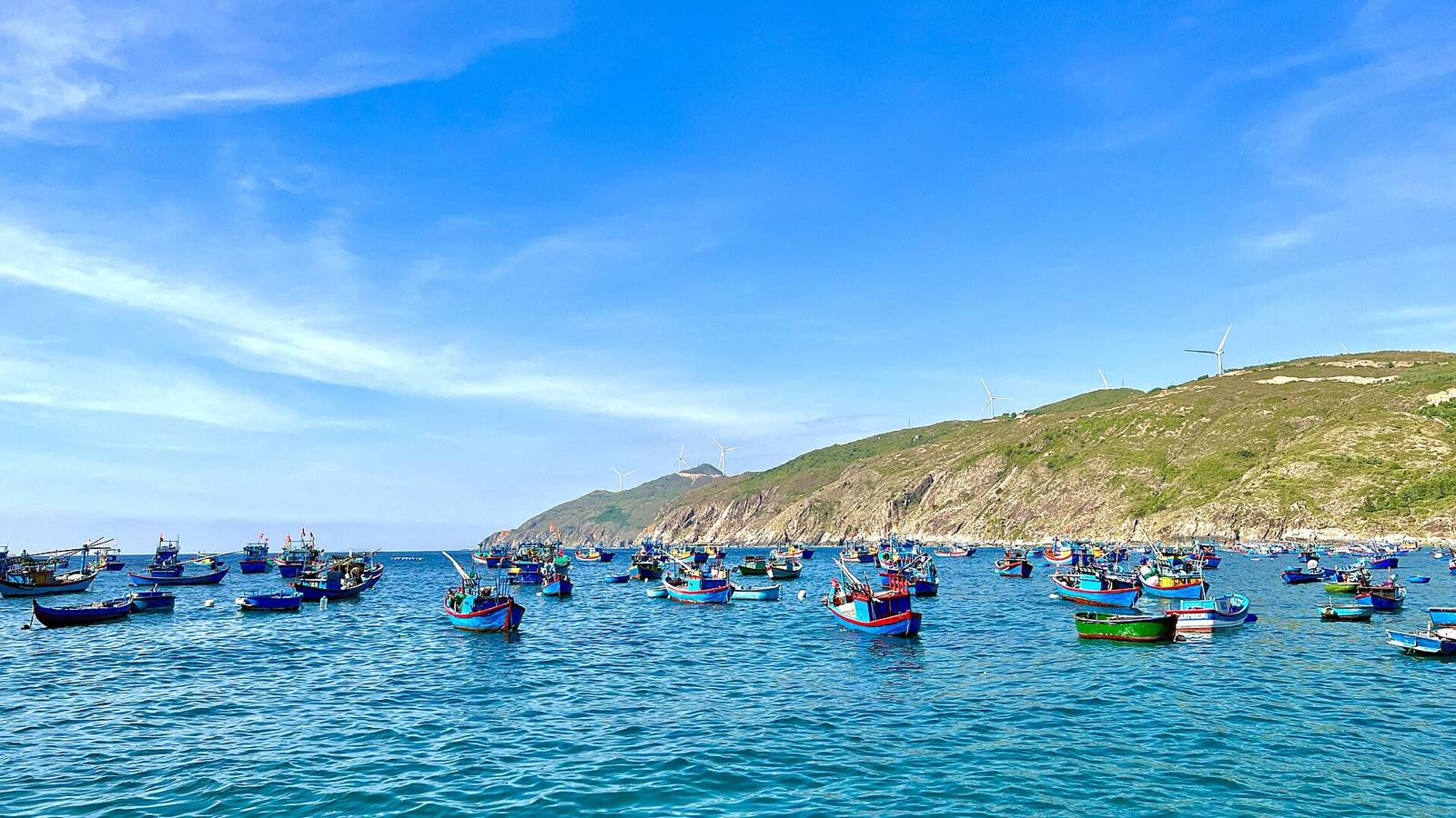 Colorful fishing boats moored off Nhon Ly near Quy Nhon, with green coastal hills under a bright blue sky