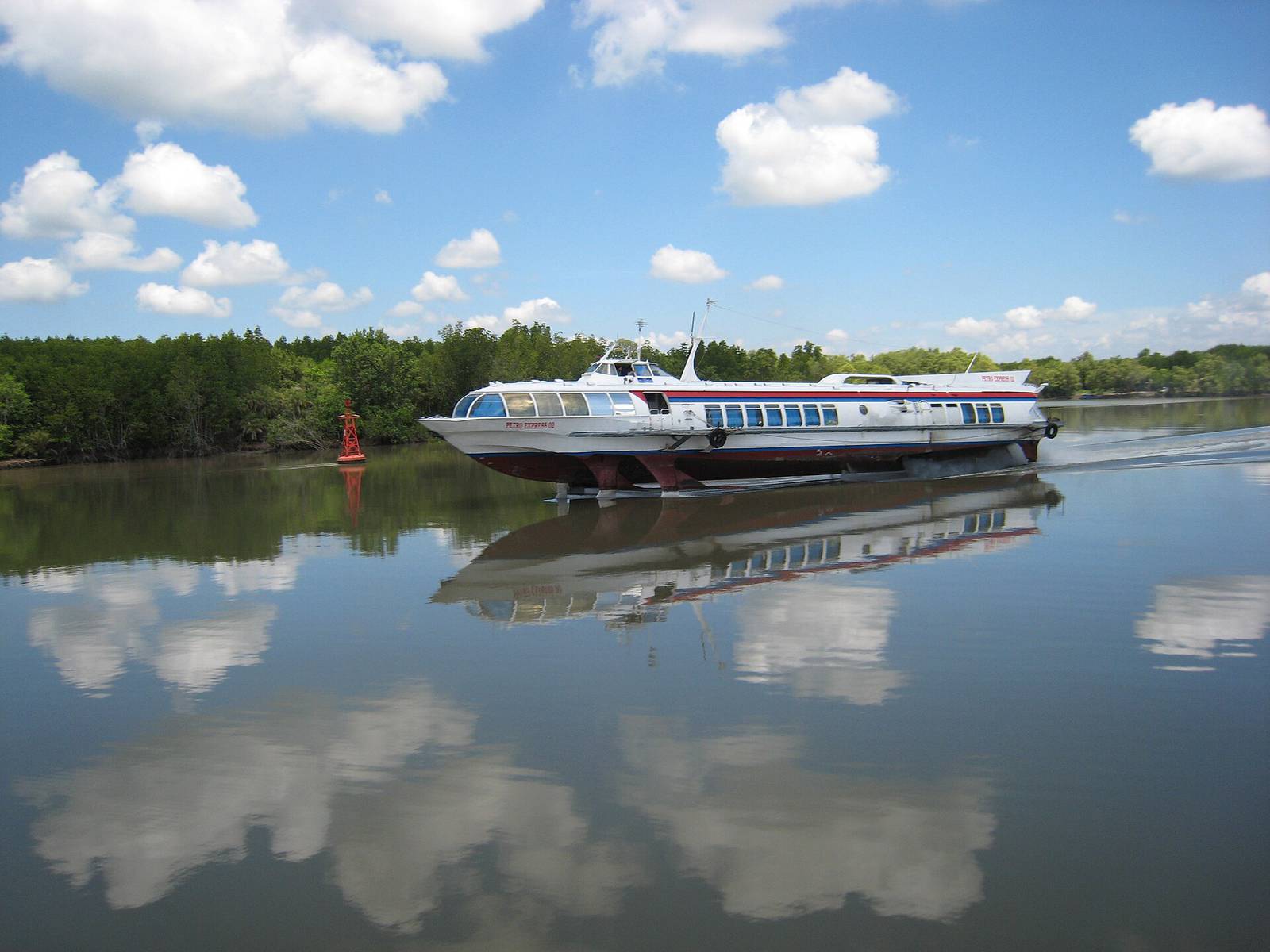 A white hydrofoil raised on its foils speeding along a calm, mangrove-lined river on the Saigon to Vung Tau run, under a blue sky with white clouds