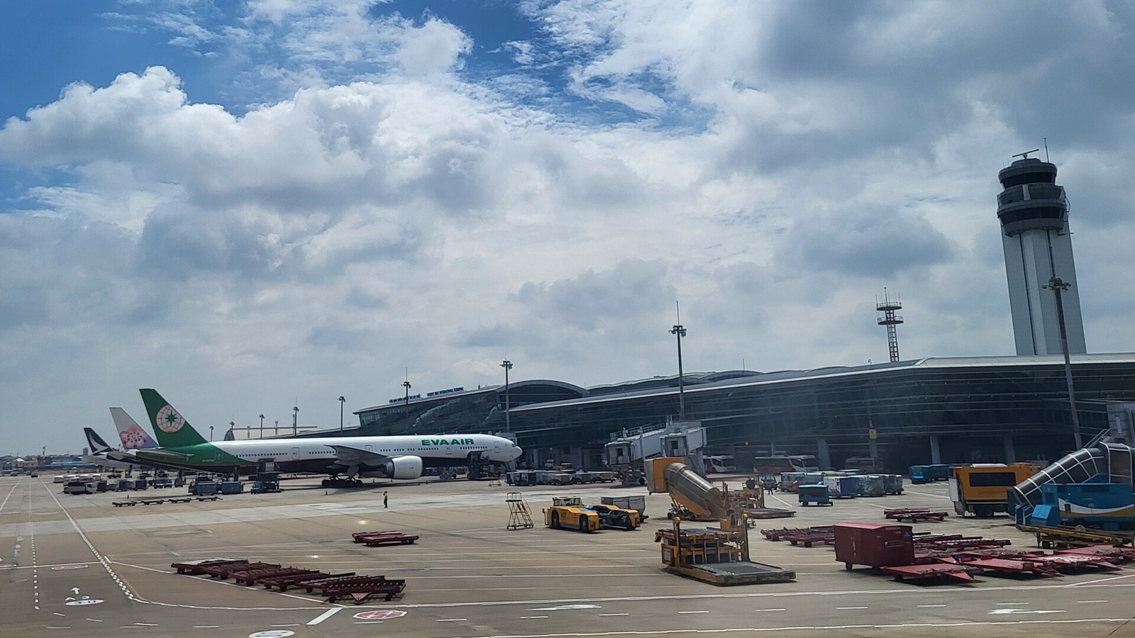 Tan Son Nhat's international terminal and control tower with an airliner at the gate under a bright, cloudy sky