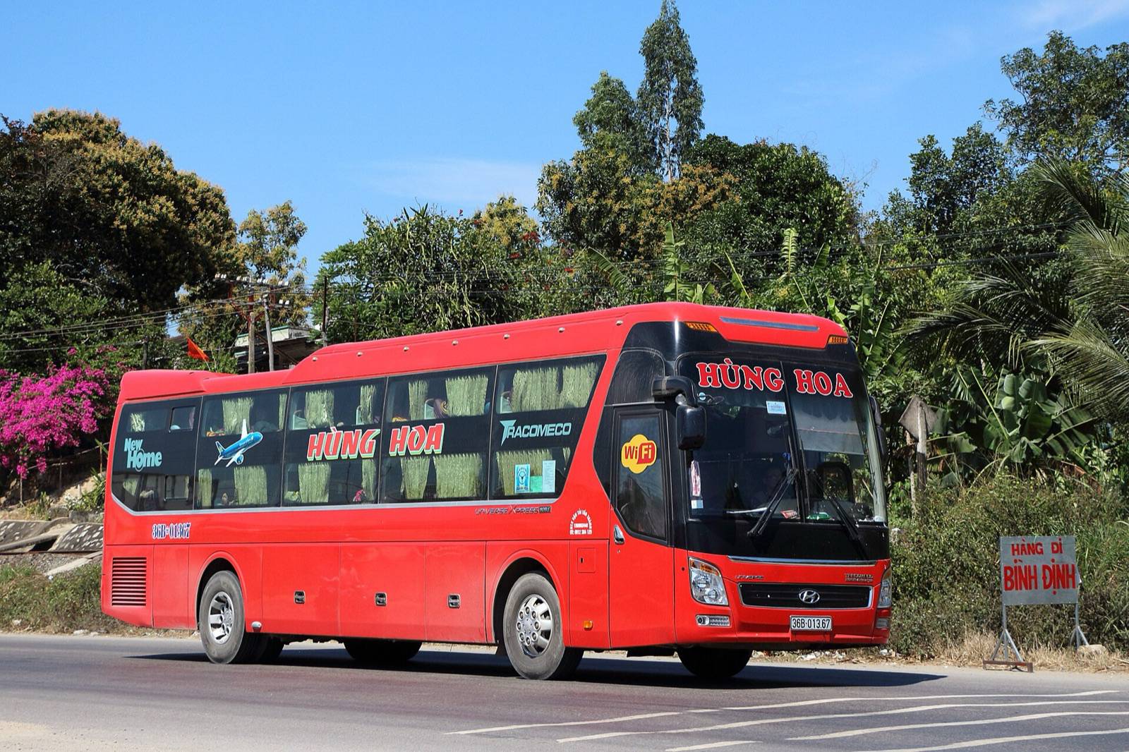 A red double-deck sleeper coach driving along a sunny tree-lined highway in Vietnam