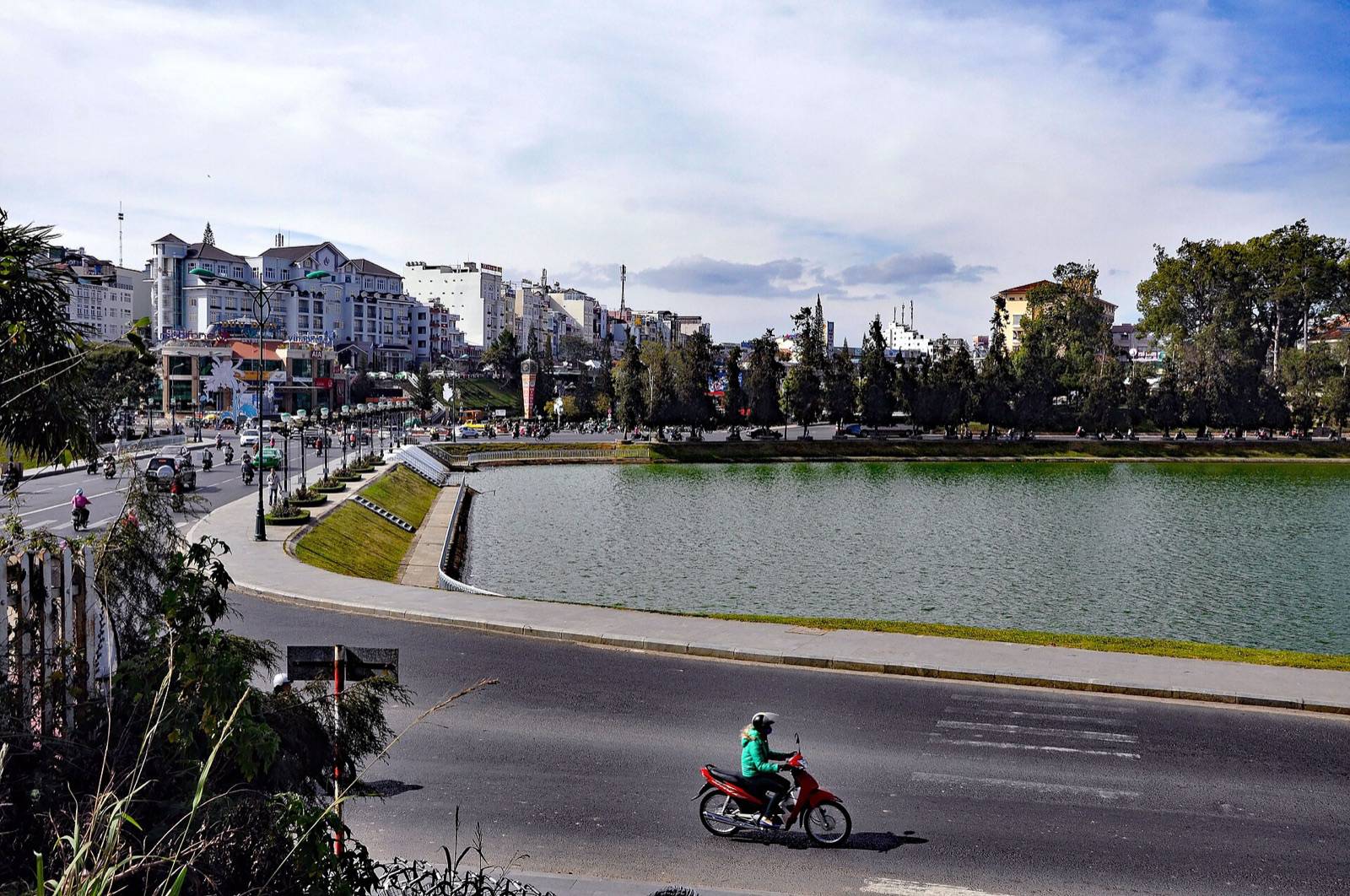 Xuan Huong Lake in central Da Lat under a bright sky, with hotels and pine trees along the shore